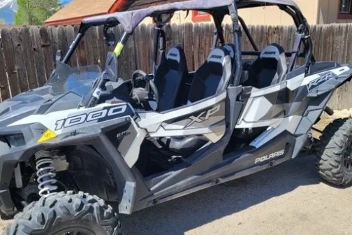 Off-road vehicle with four seats parked outside by a fence.