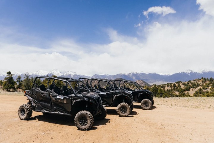 Three off-road vehicles on a dirt path with mountains in the background.